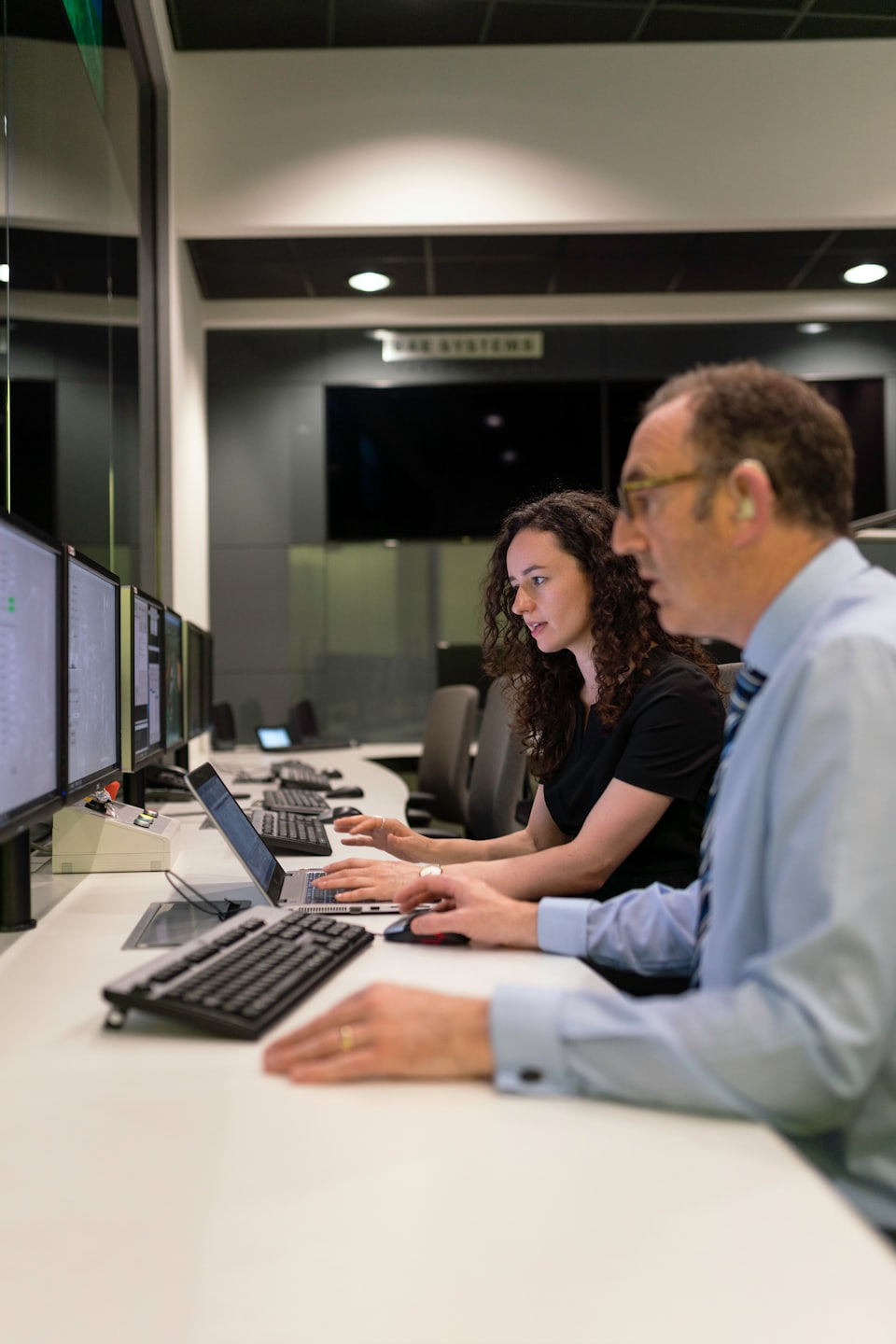 Two professionals collaborate on computers in a modern office.